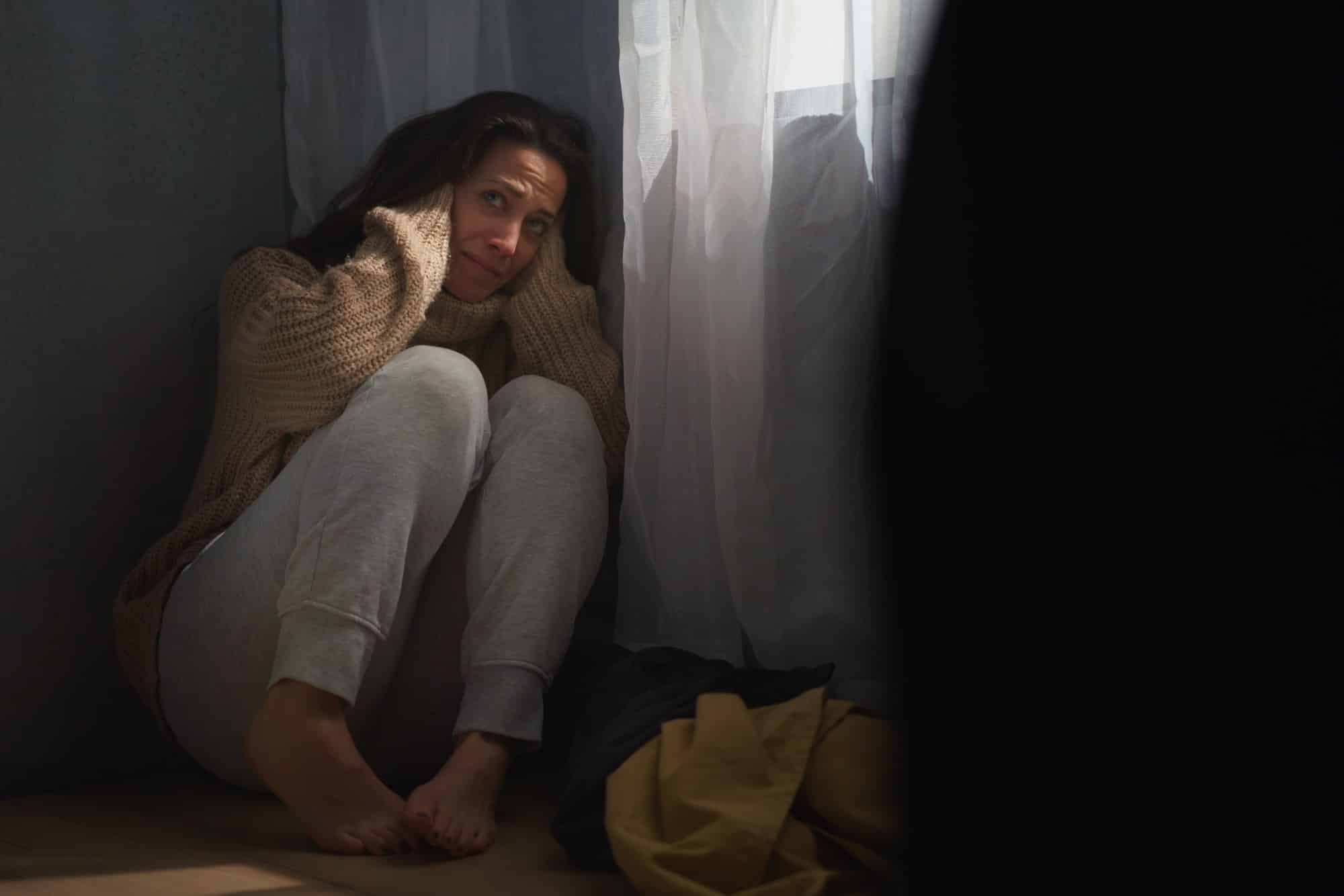 Scared woman sitting on ground and covering her head in fear of domestic violence