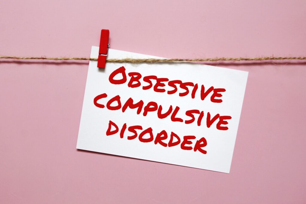 Sticker with the inscription obsessive compulsive disorder hanging on a rope on a pink background