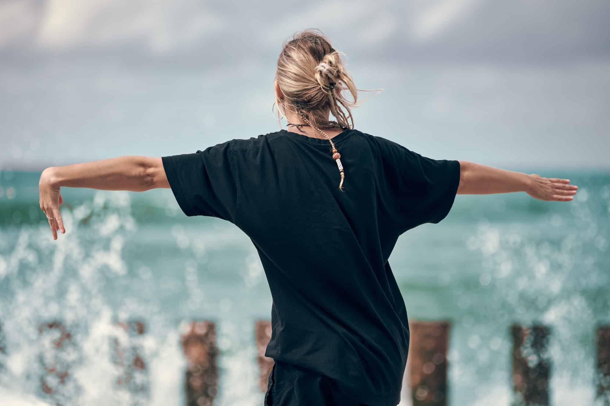 Woman dancing to music on sea coast, rear view, dancers at outdoor art performance music festival